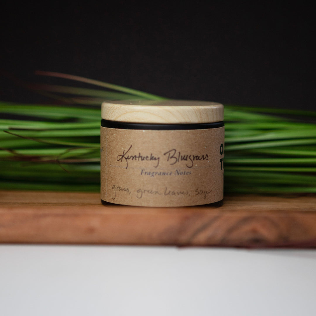 Candle jar with a Kentucky Bluegrass on a wooden surface with green grass in the background